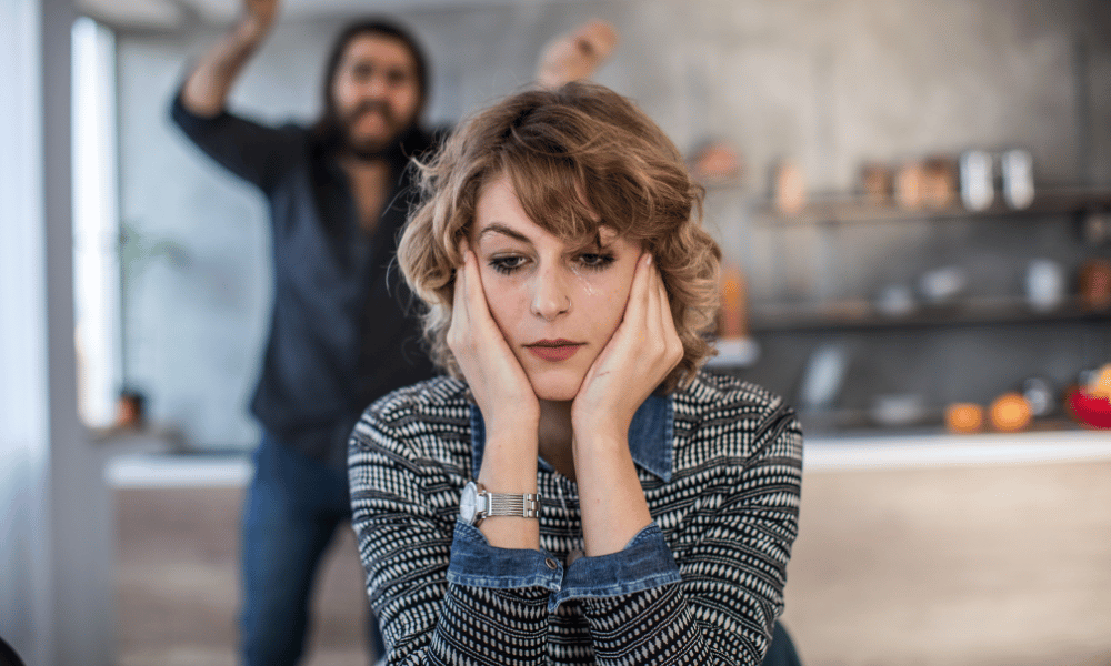 Woman crying while her addict husband yells from behind her