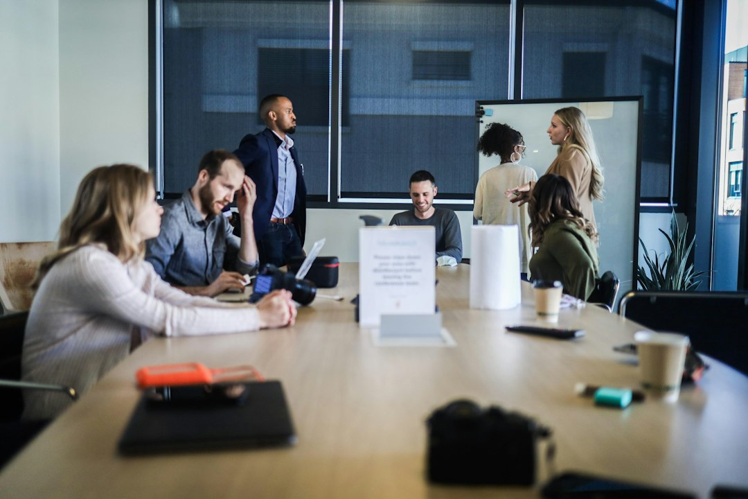 A diverse group of professionally dressed people gathered around a table in a bright, modern space, engaged in a collaborative discussion about owner advocacy.